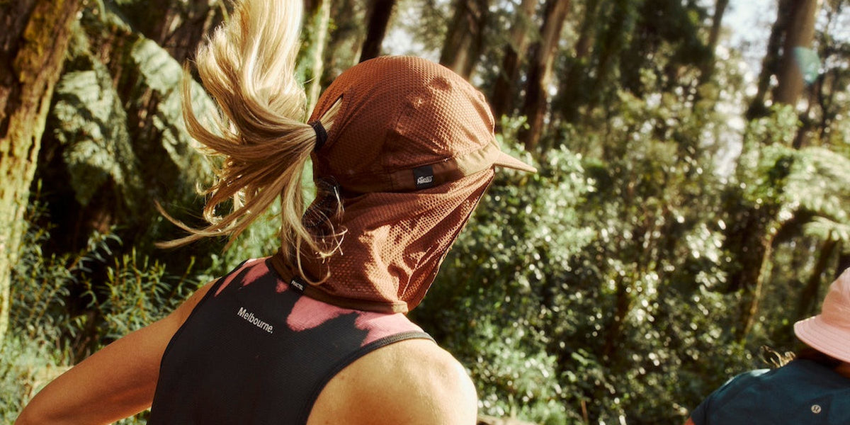 Runner in a rust Fractel seasonal legionnaire running hat with a neck cape in a fern forest