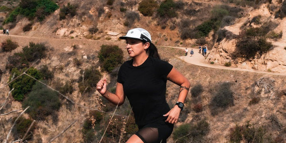 Runner in a white Fractel flowmesh running cap and black tee on a dry canyon trail