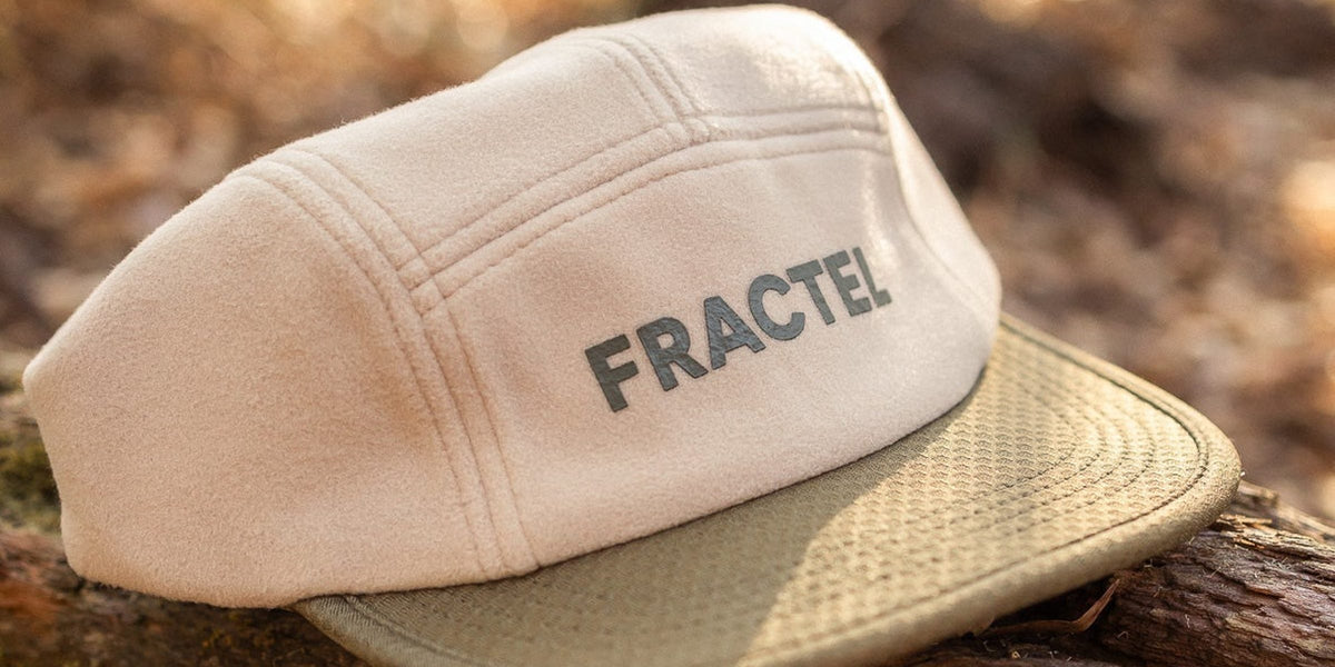 Cream Fractel cap in Polartec Wind Pro fabric with grey FRACTEL lettering resting on a log
