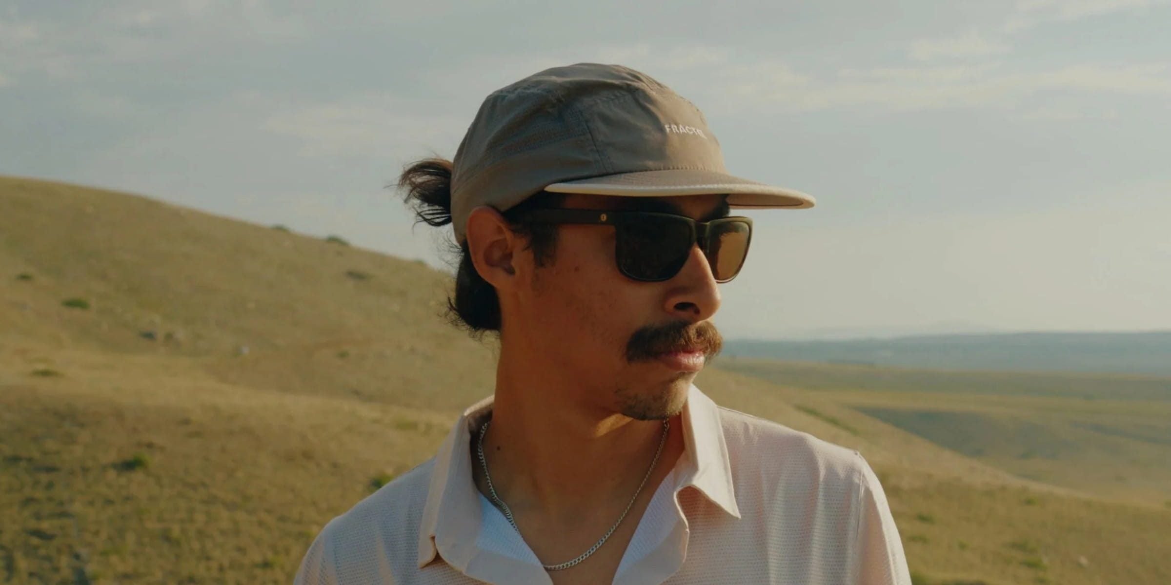 Man in sunglasses wearing a grey Fractel cap from our range of running hats, on a grassy hillside