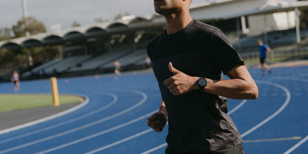 Runner in a black Fractel tee and watch on a blue athletics track, from the r series premium race cap collection