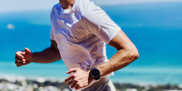 Man in a white Fractel running tee mid-stride above the ocean, part of our mens running apparel range