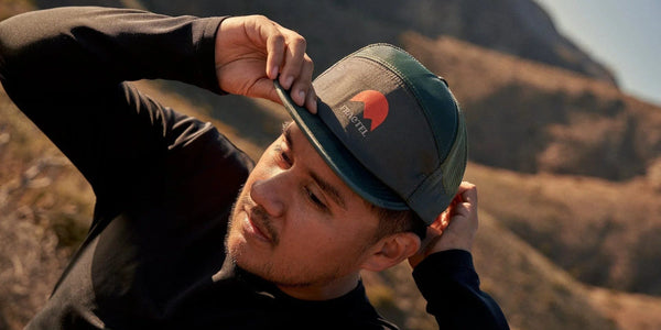 Man adjusting a dark Fractel cap with a sunrise logo, one of our hats for big heads, on a hillside