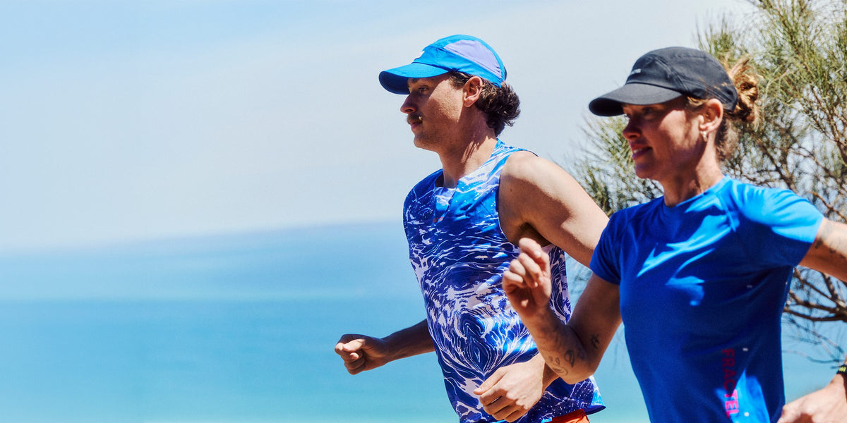 Two runners in blue Fractel caps and singlets from the velocity running collection beside the sea