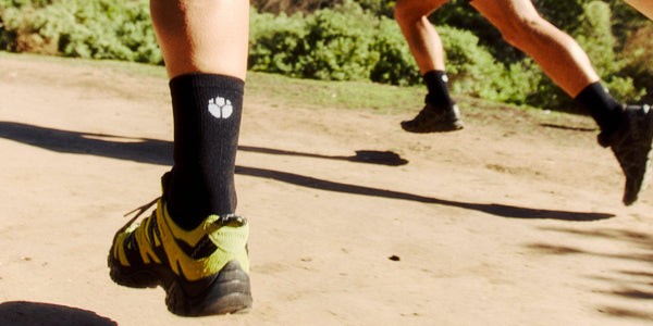 Close-up of a runner's black Fractel womens running socks with a white logo on a dirt trail