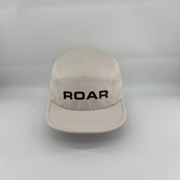 A light beige 5-panel cap with 'ROAR' embroidered in dark purple across the front, set against a plain light gray background.