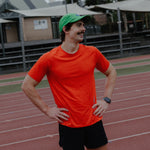 Male wearing an orange shirt and green cap on a track