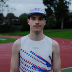 Male wearing a white singlet with blue and red patterns and a cap on a track field.