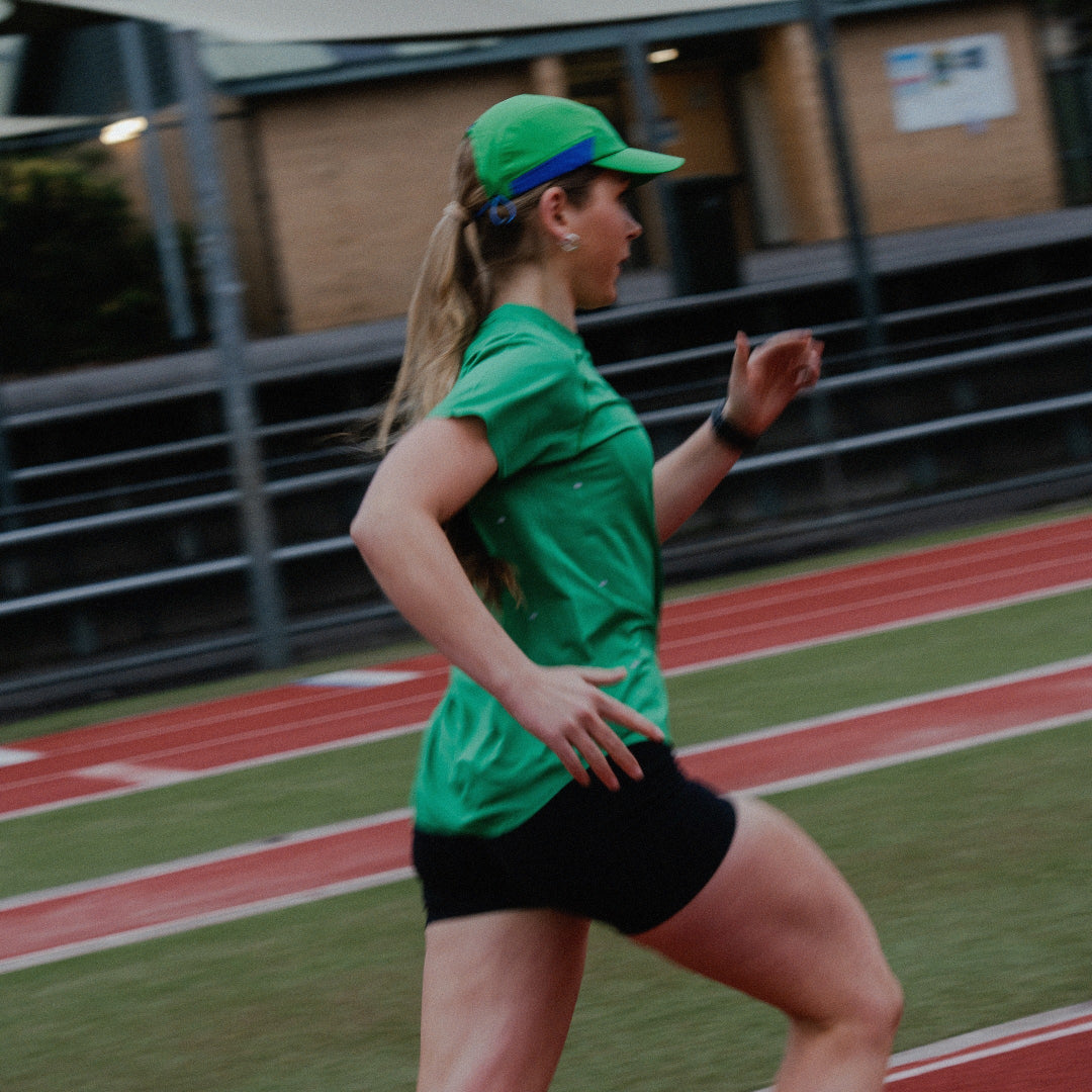 Female running on a track wearing a green shirt and cap.