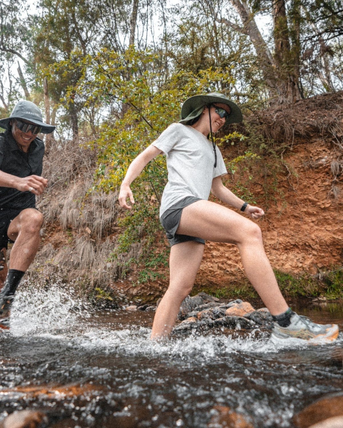 Trail runner crossing a creek in a Fractel hiking running hat with a neck cape