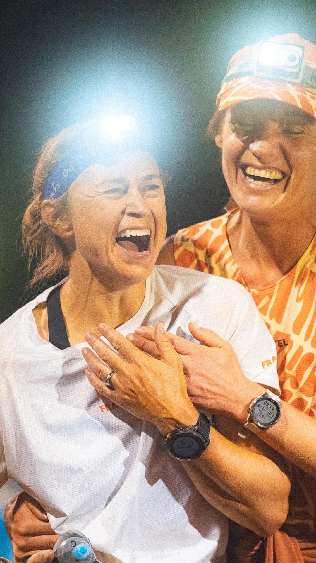 Two people laughing together, one wearing a headlamp.