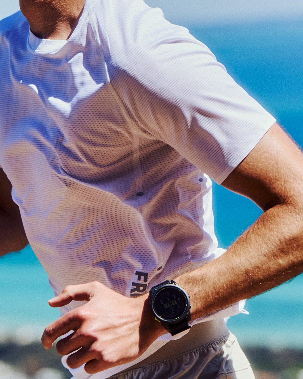 Mens running tee in white with FRACTEL lettering at the hem, worn on a coastal run