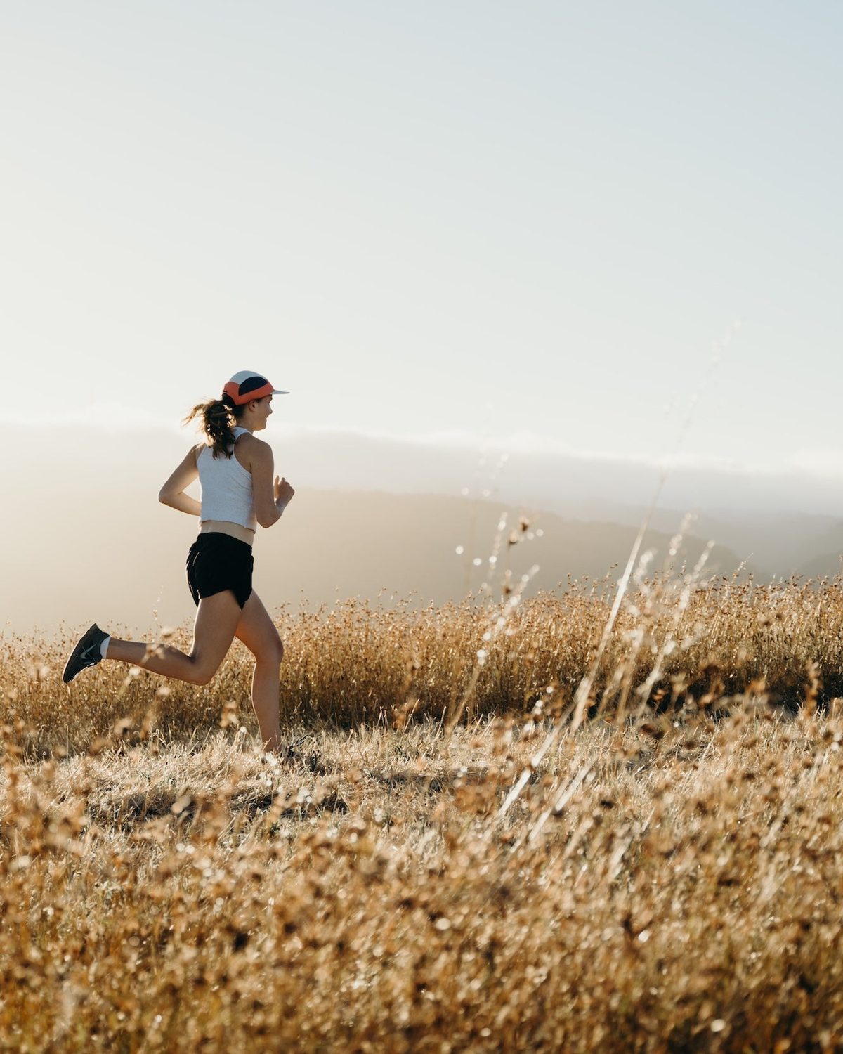 Summer running gear: runner in a Fractel visor on a sunlit grassy hill